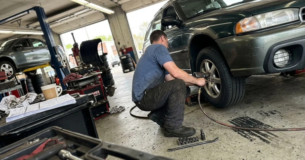 Technician mounting a tire on a machine, New Britain shop bay, candid