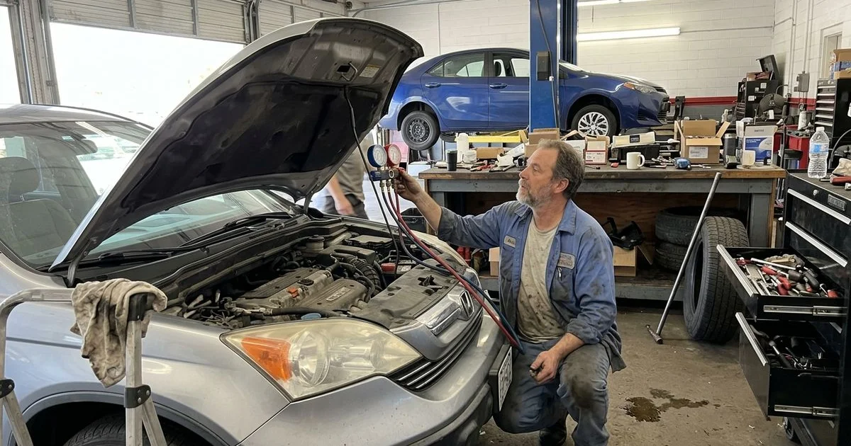 Technician connecting A/C gauges to a car under the hood, New Britain shop, candid