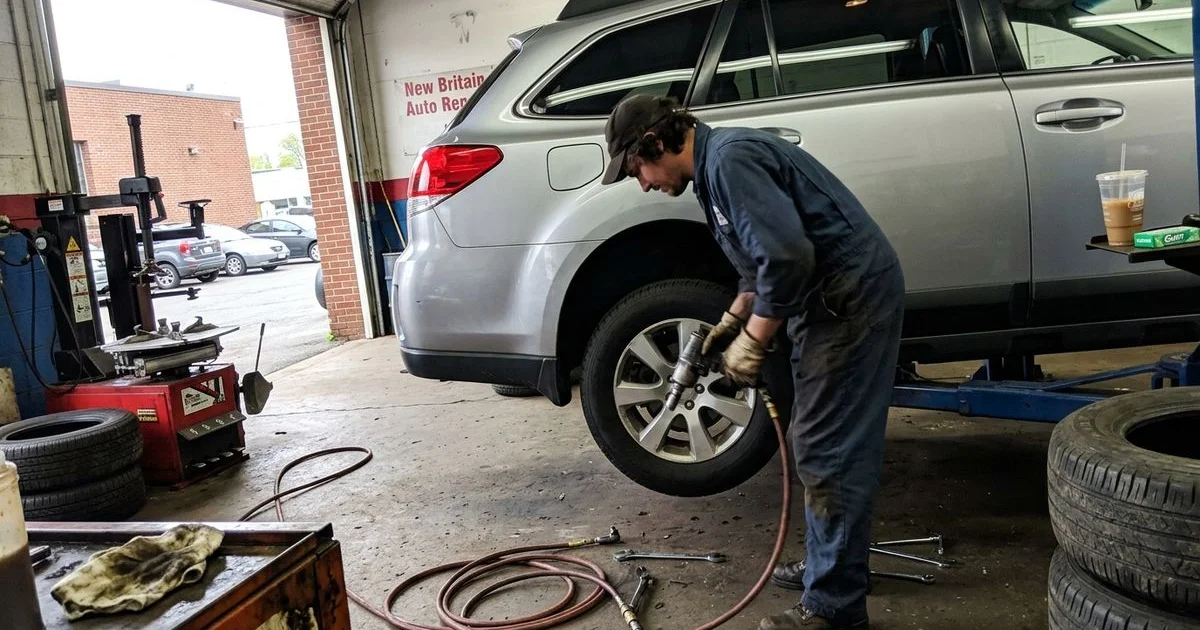 Technician rotating tires on a lifted car, New Britain shop, candid